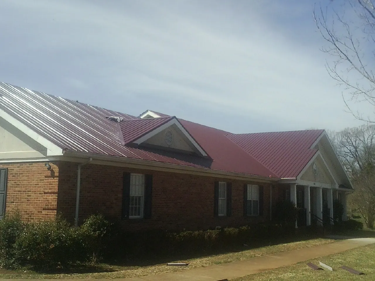 Red metal roof with gabled entries on a long brick building, from a Hail Damage Roof Repair job in Belgrade