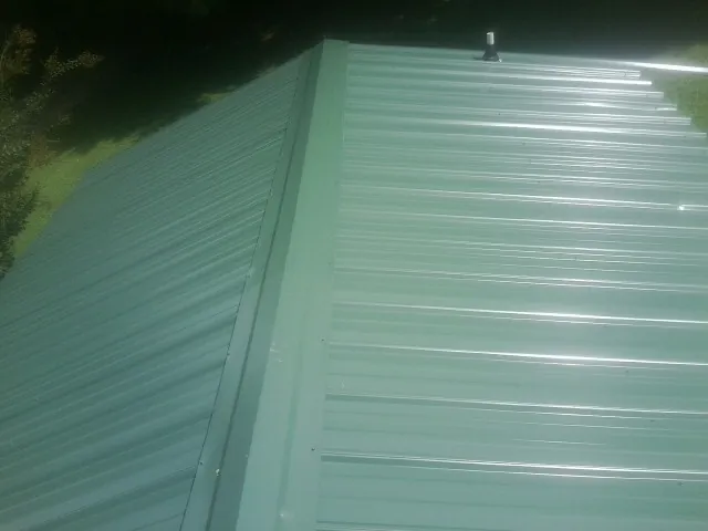 New green metal panels meeting at the ridge of a roof — Flat Roof Repair work by our crew in Belgrade