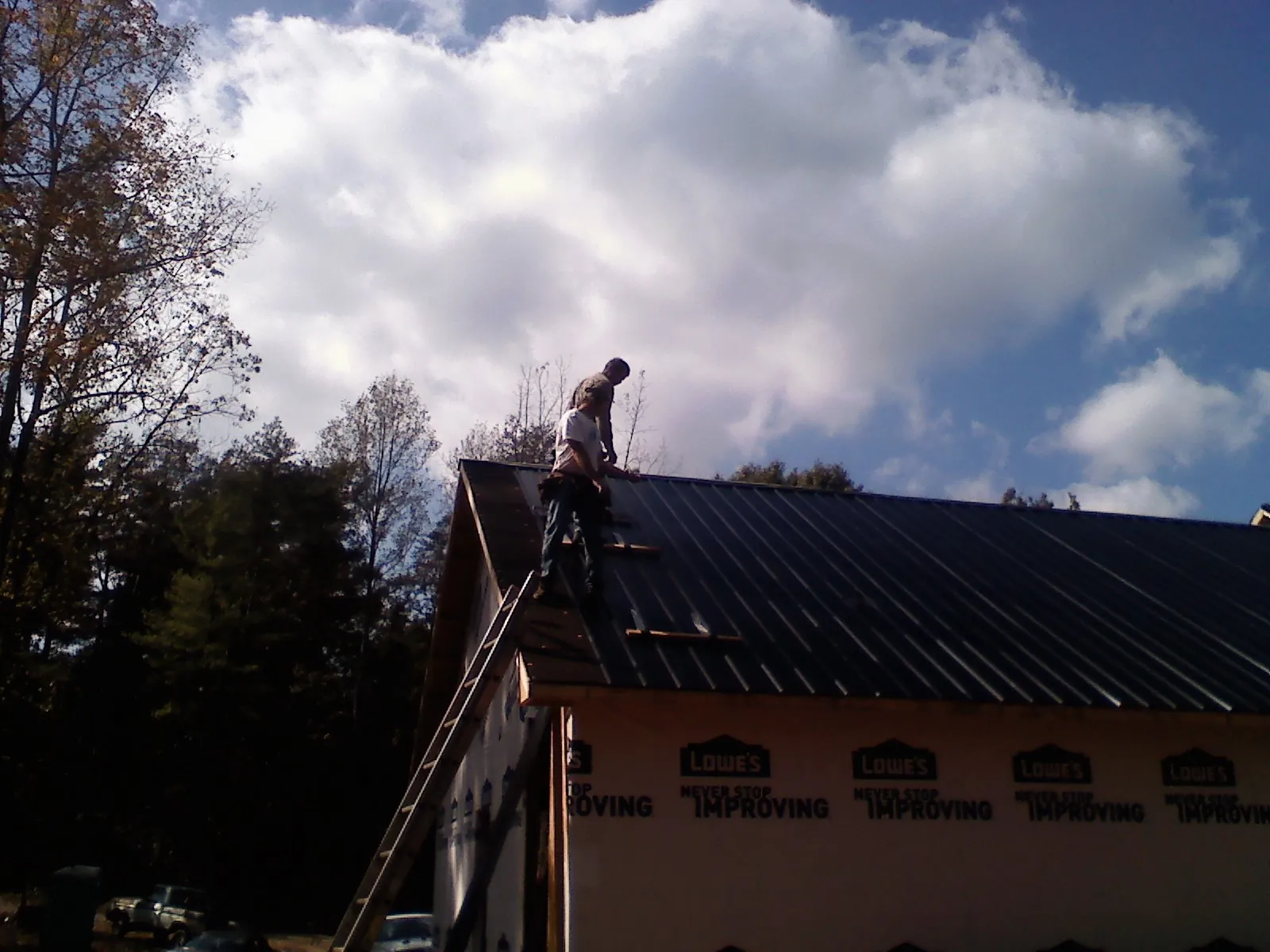 Roofer fastening dark metal panels high against a cloudy sky, from a Roof Inspection job in Belgrade